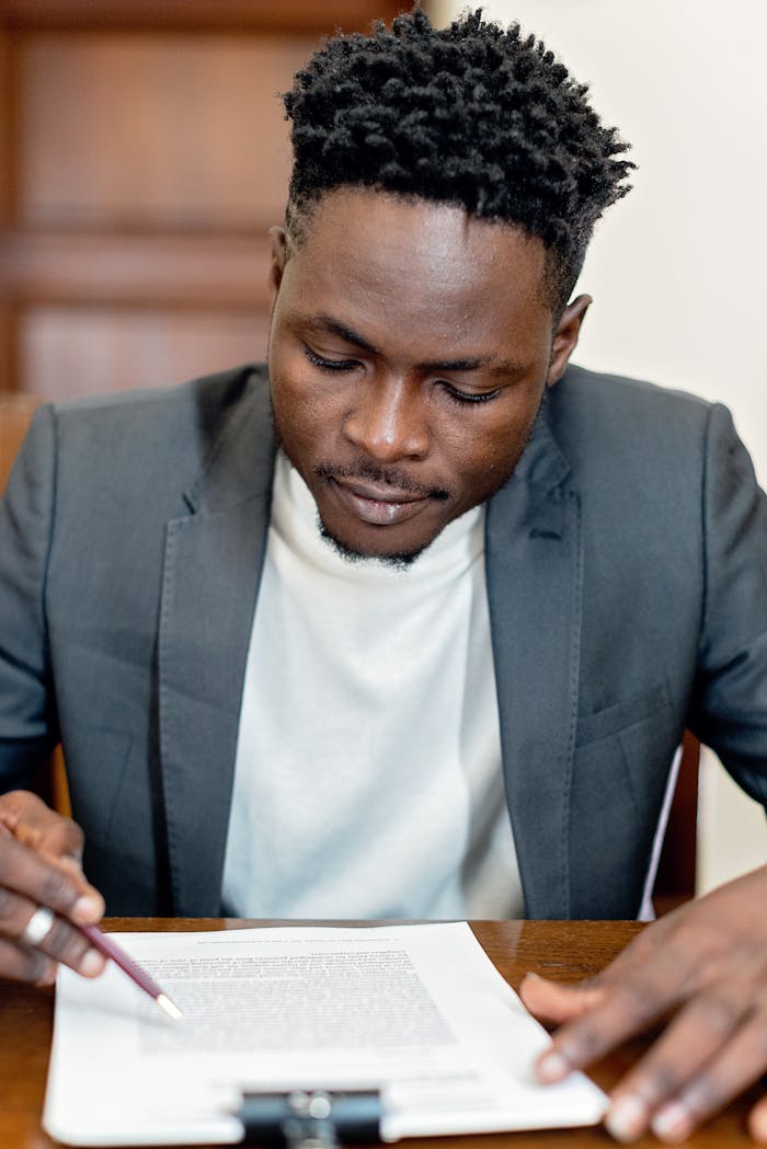A focused businessman in a gray suit closely reviewing legal paperwork at a desk indoors.